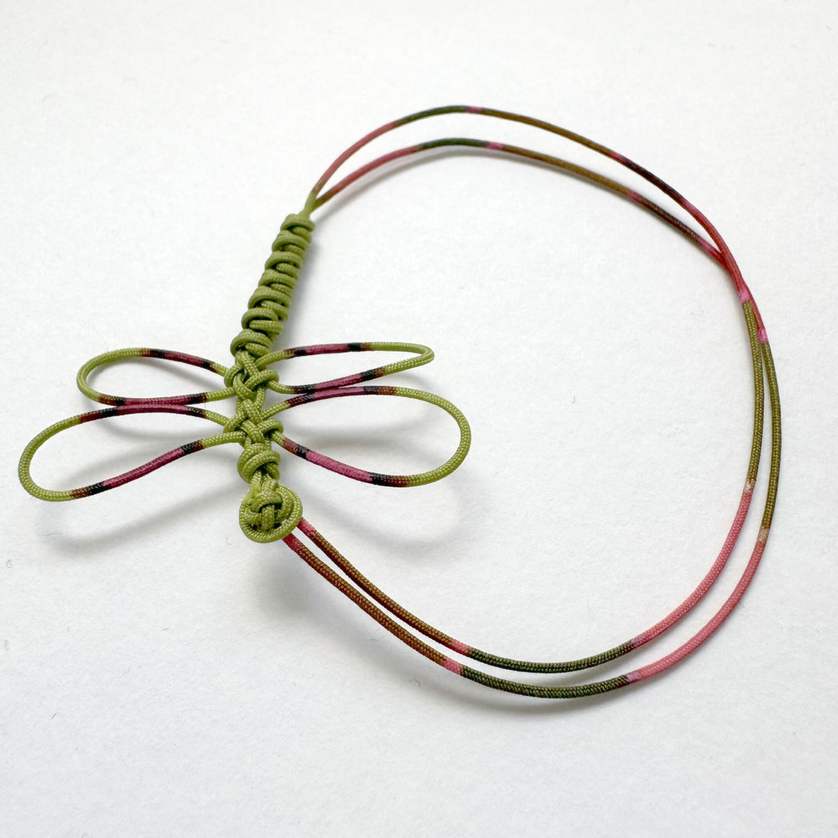 Bracelet cordon vert tressé avec motif noué multicolore rouge-brun et rose clair.