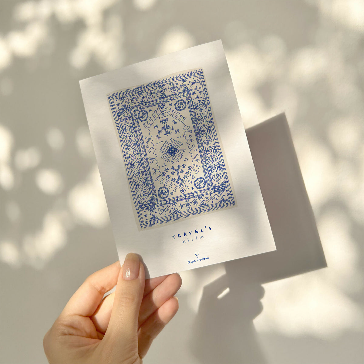 Carte illustrée bleue motif kilim encadré, tenue par une main