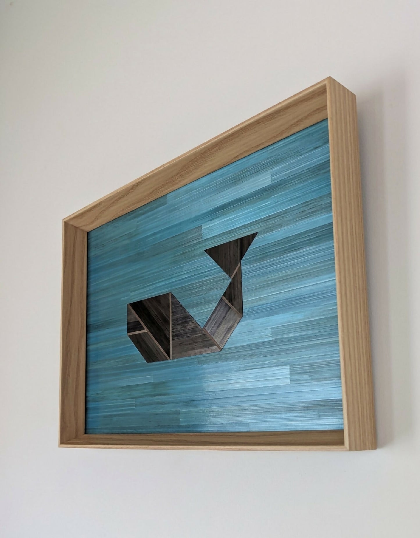 Tableau en marqueterie bleu, formes géométriques anthracite, cadre bois clair.
