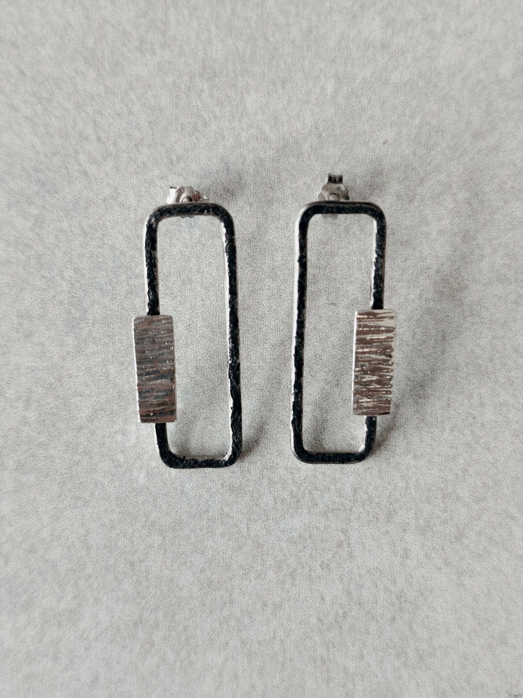 Boucles d’oreilles rectangulaires, plaque striée et bordure foncée, fixation visible