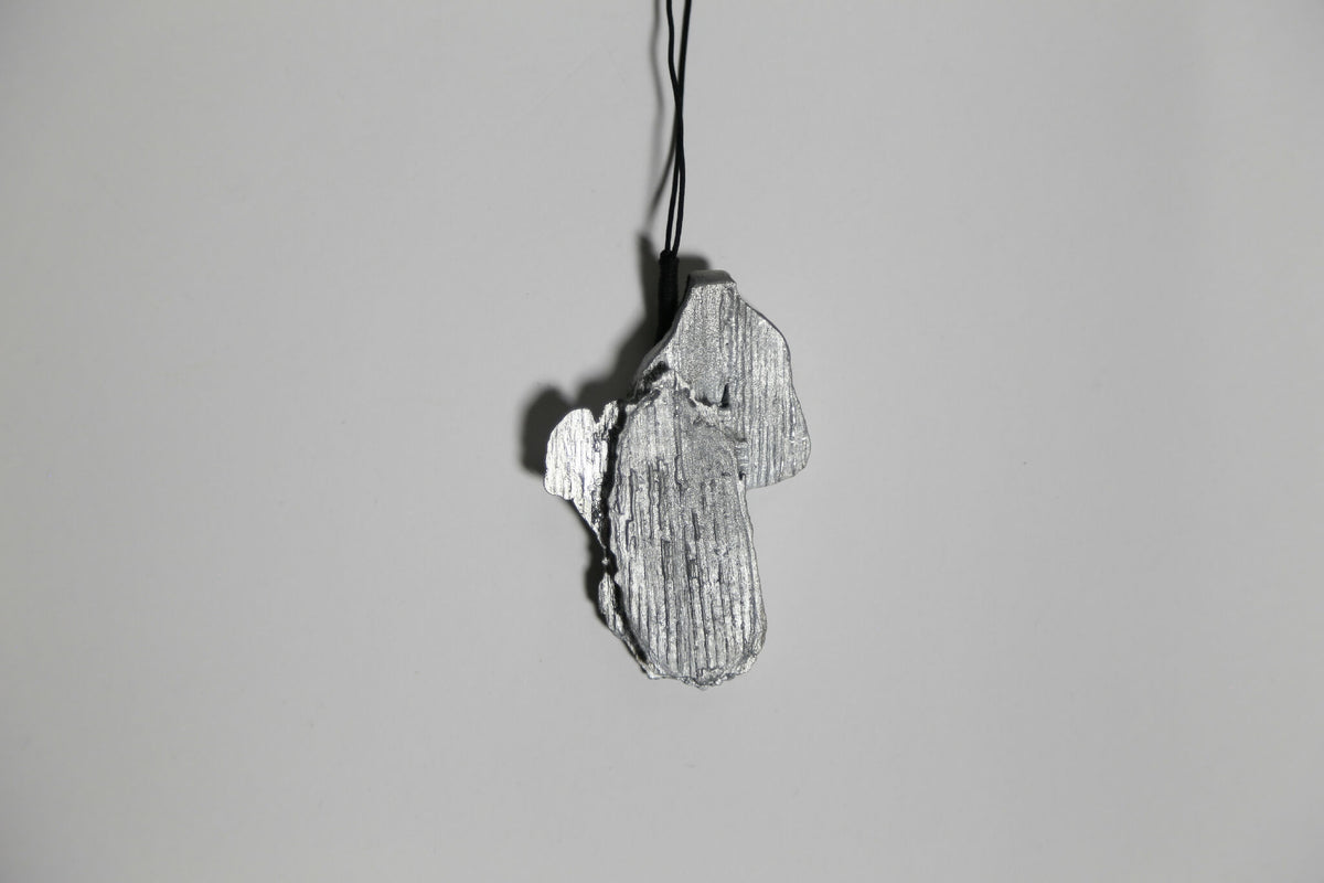 Pendentif gris argenté en forme de feuille, vue de dessus, sur cordon.