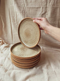 Assiette creuse en céramique beige à bord brun, motif texturé, pile de bols