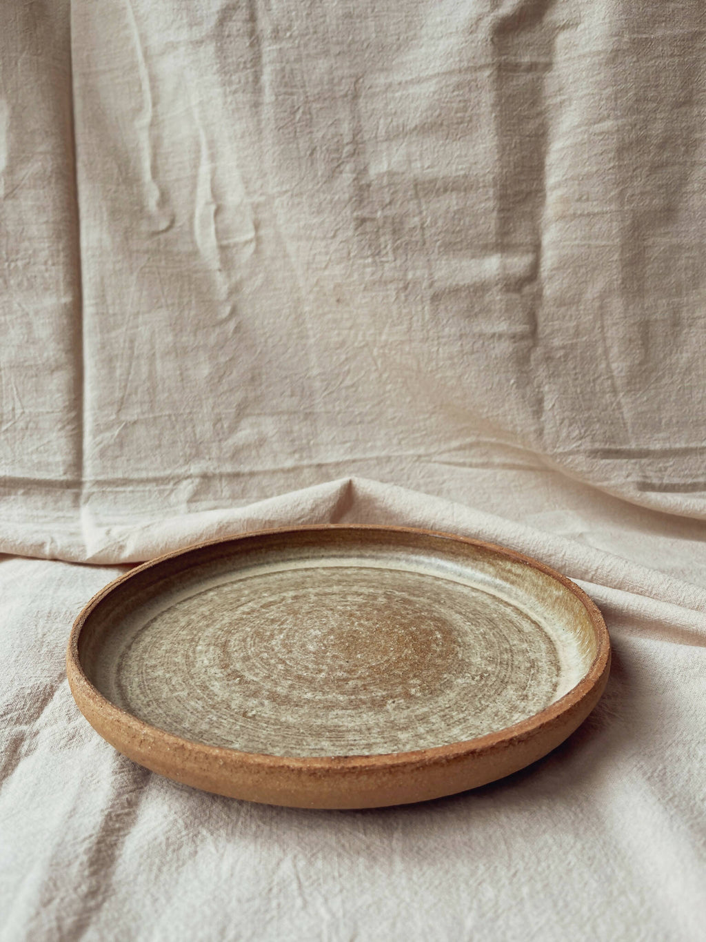 Assiette creuse en céramique beige à bord brun, vue de dessus, finition texturée