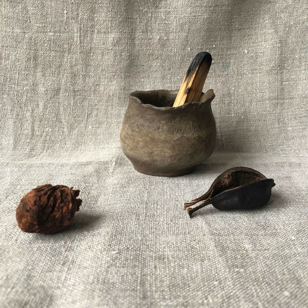 Petit pot en terre cuite gris foncé, forme arrondie évasée, surface texturée.