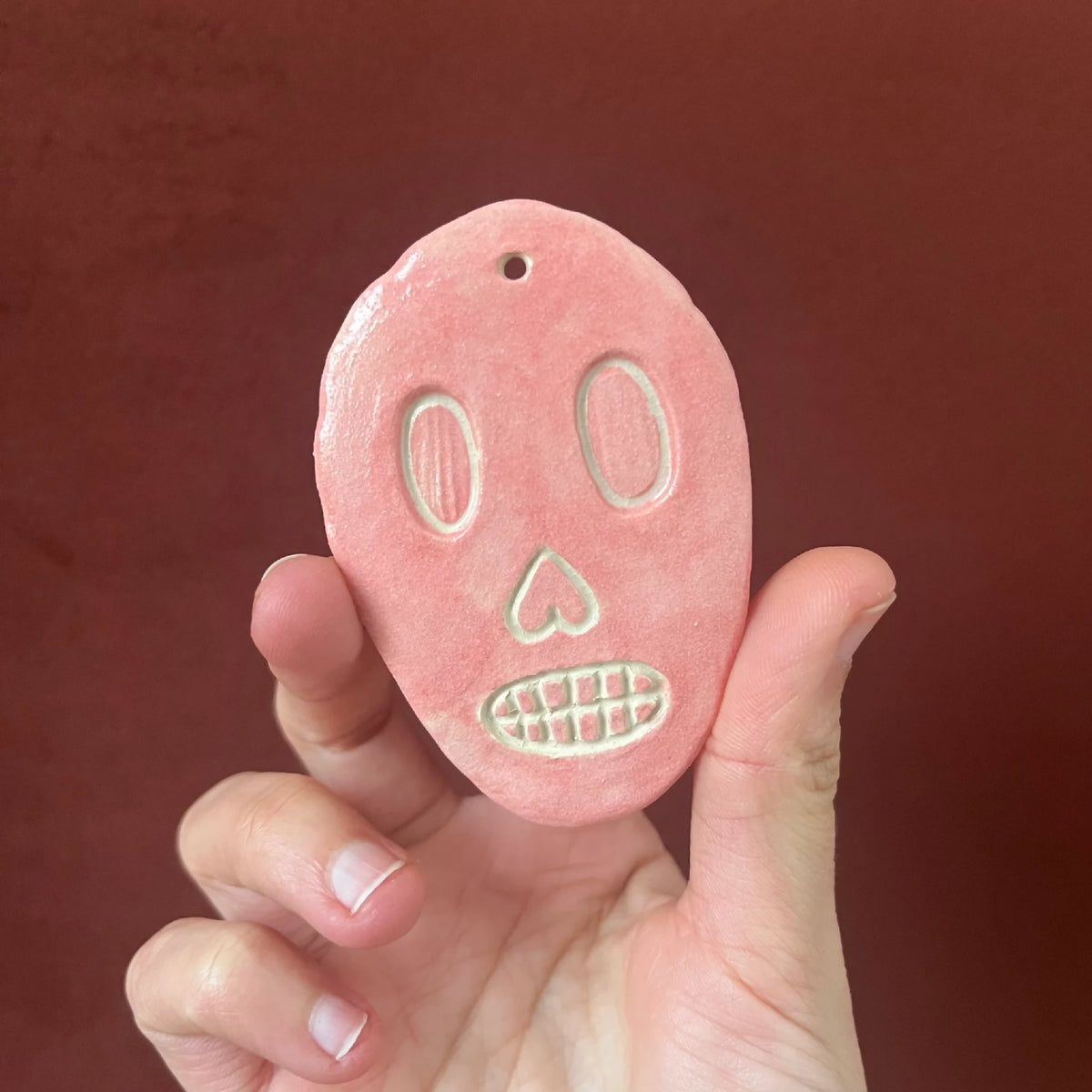 Crâne en céramique rose, visage souriant avec yeux verts et dents blanches