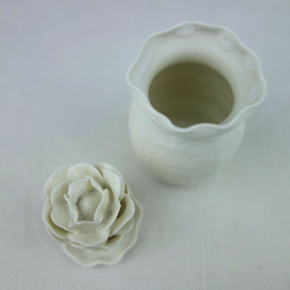Vase en céramique blanc avec ouverture supérieure; petite fleur en relief à côté.
