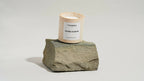 Bougie parfumée Cannelya Vanille Ambrée sur bloc de pierre grise, pot beige