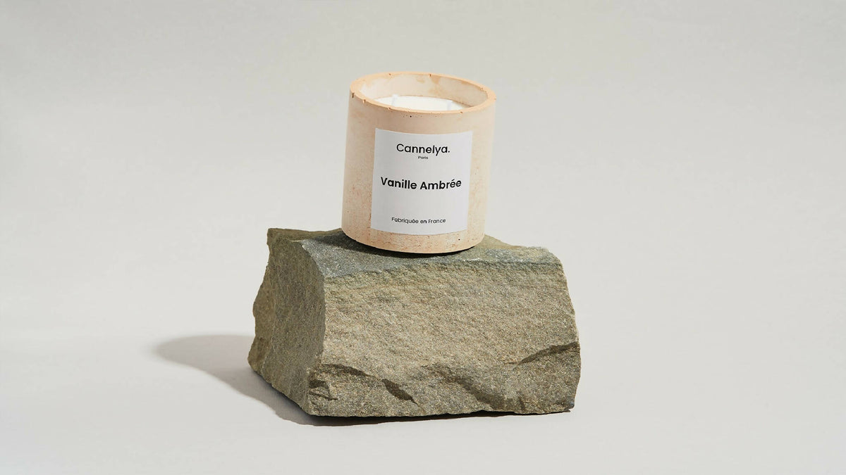 Bougie parfumée Cannelya Vanille Ambrée sur bloc de pierre grise, pot beige