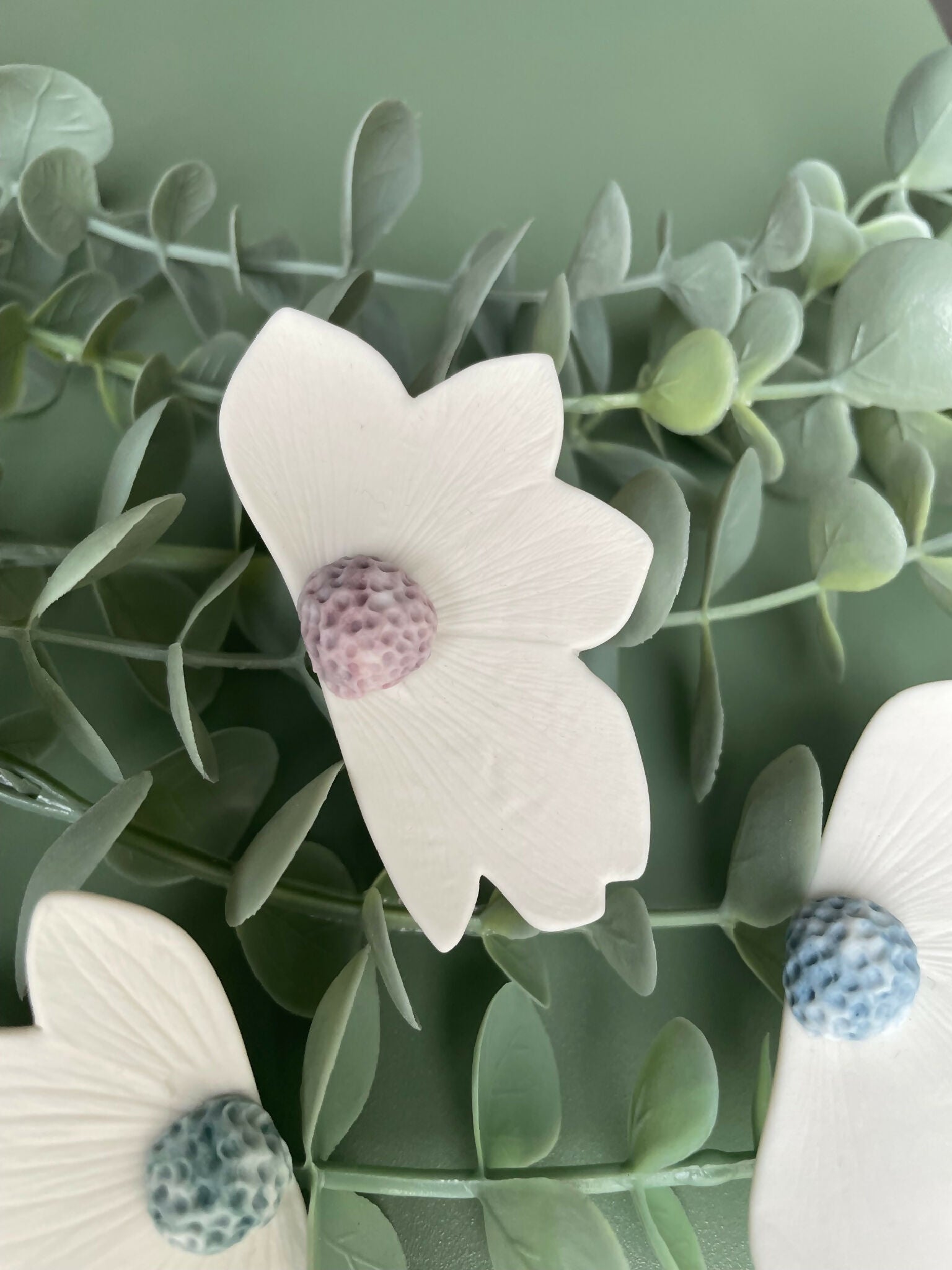 Broche florale en porcelaine aimantée, pétales blancs, centre violet clair texturé.