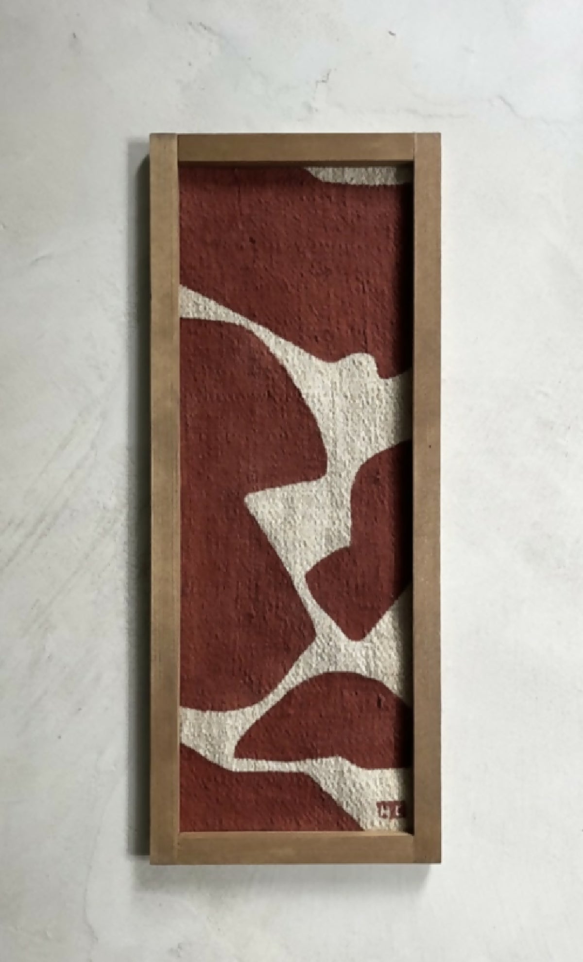 Tableau abstrait en cadre bois brun clair, formes beige sur fond bordeaux.