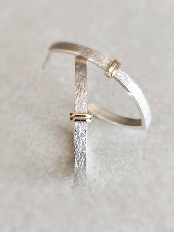 Boucle d’oreille courbe argentée texturée avec fermoir doré, vue rapprochée