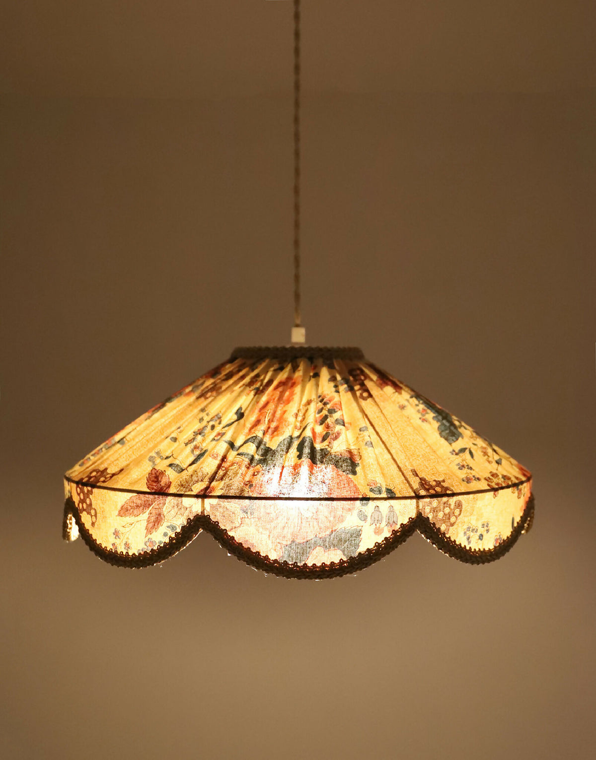 Abat-jour suspendu à motif floral, bord festonné et lumière visible à travers le tissu