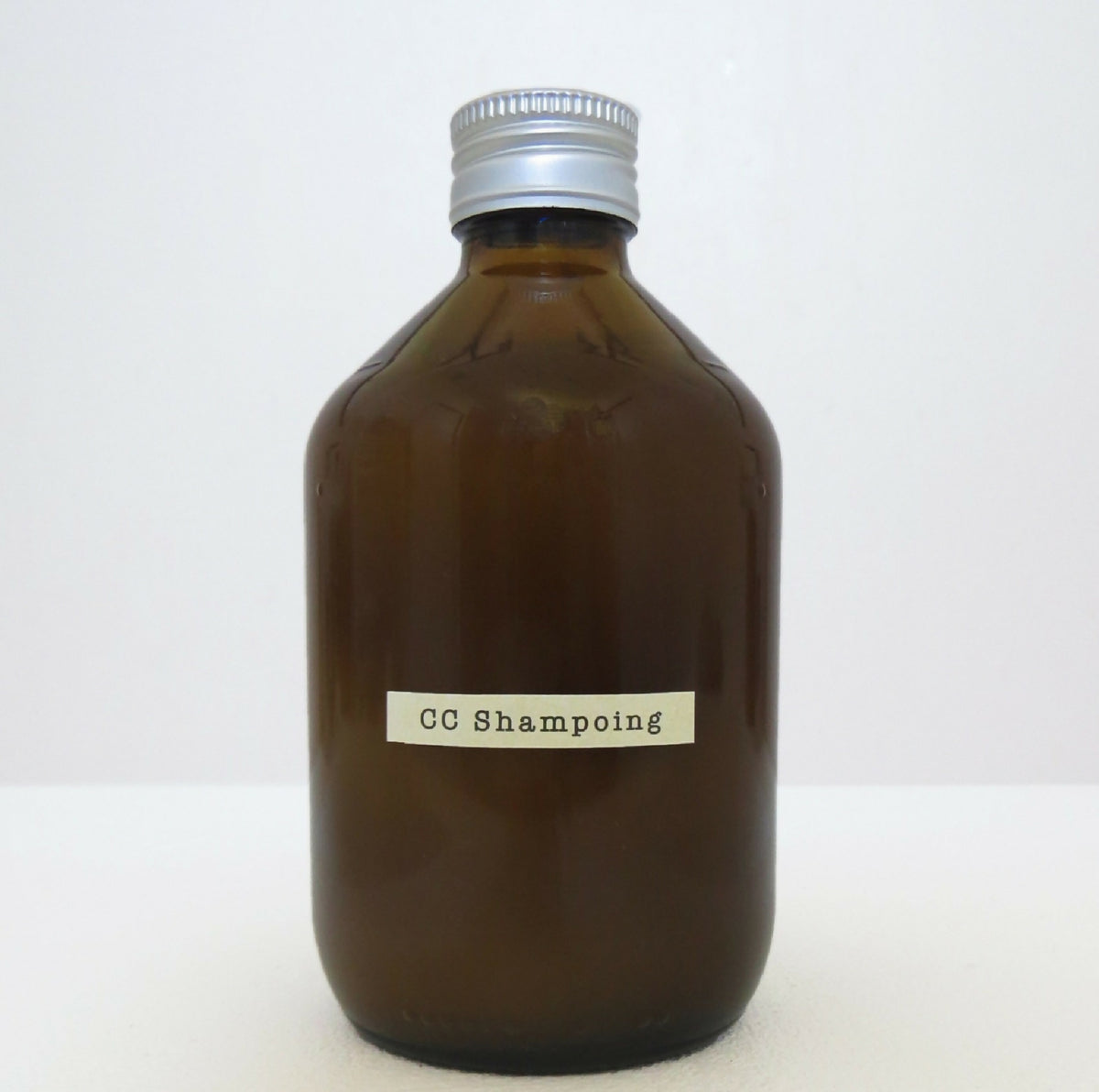 Flacon de shampoing en verre brun, bouchon cannelé et étiquette rectangulaire blanche.