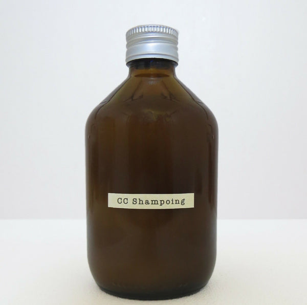 Flacon de shampoing en verre brun, bouchon cannelé et étiquette rectangulaire blanche.