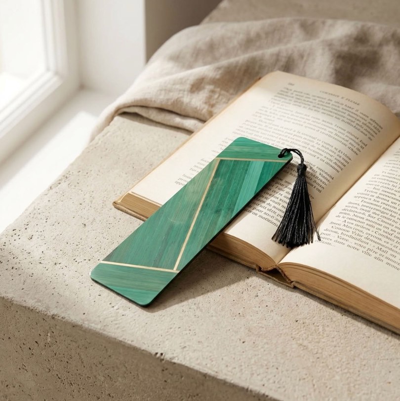 Marque-page marqueterie de paille verte, frange noire, sur livre ouvert.
