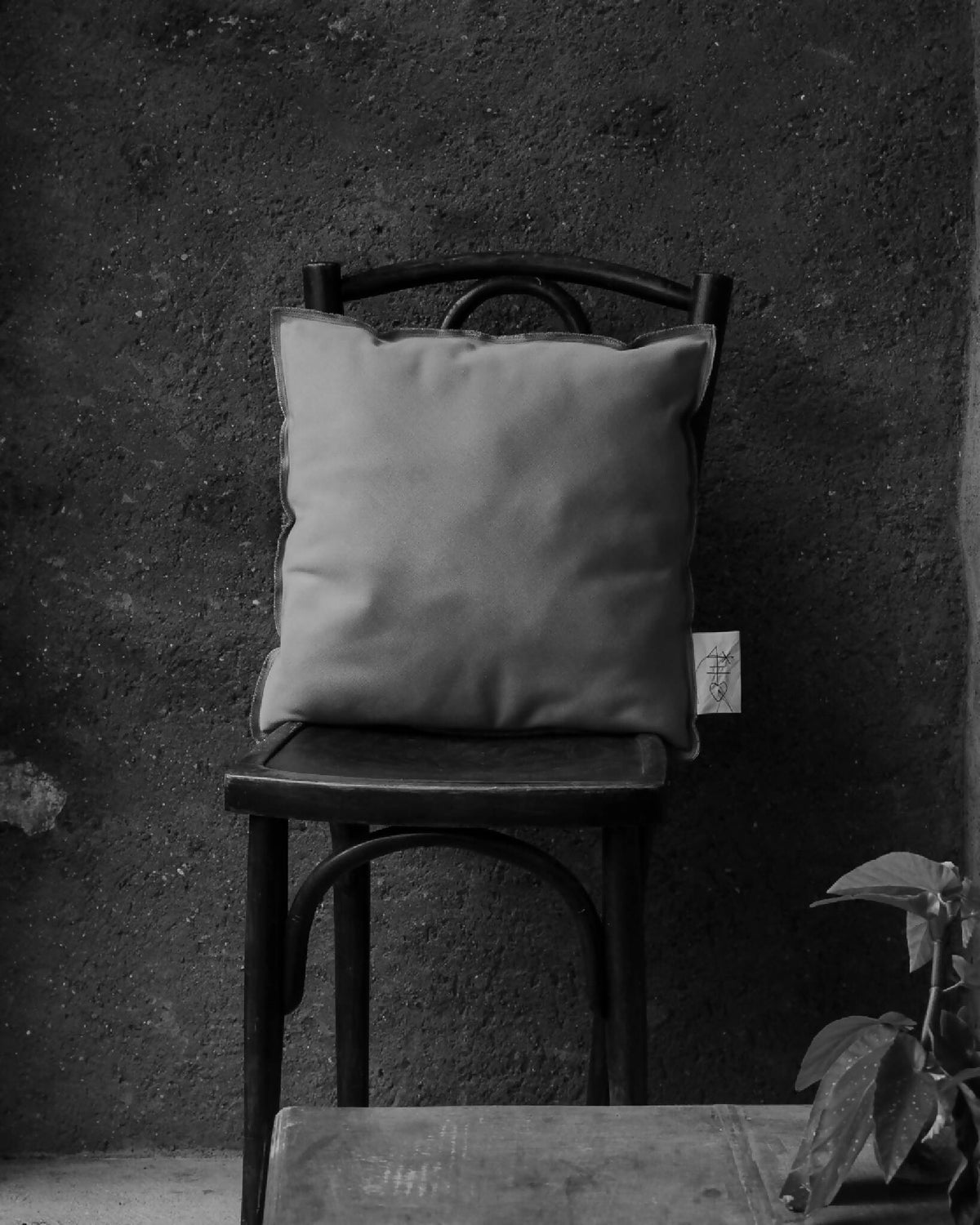 Coussin carré gris clair sur chaise, housse lisse avec étiquette