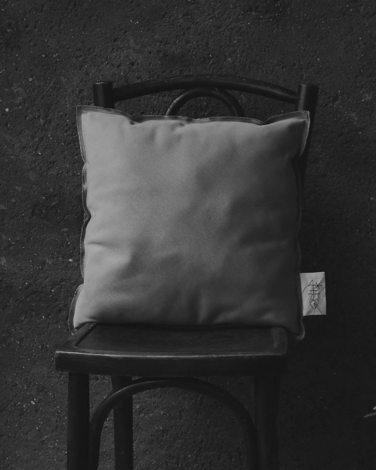 Coussin carré gris clair sur chaise, vue de face, étiquette visible