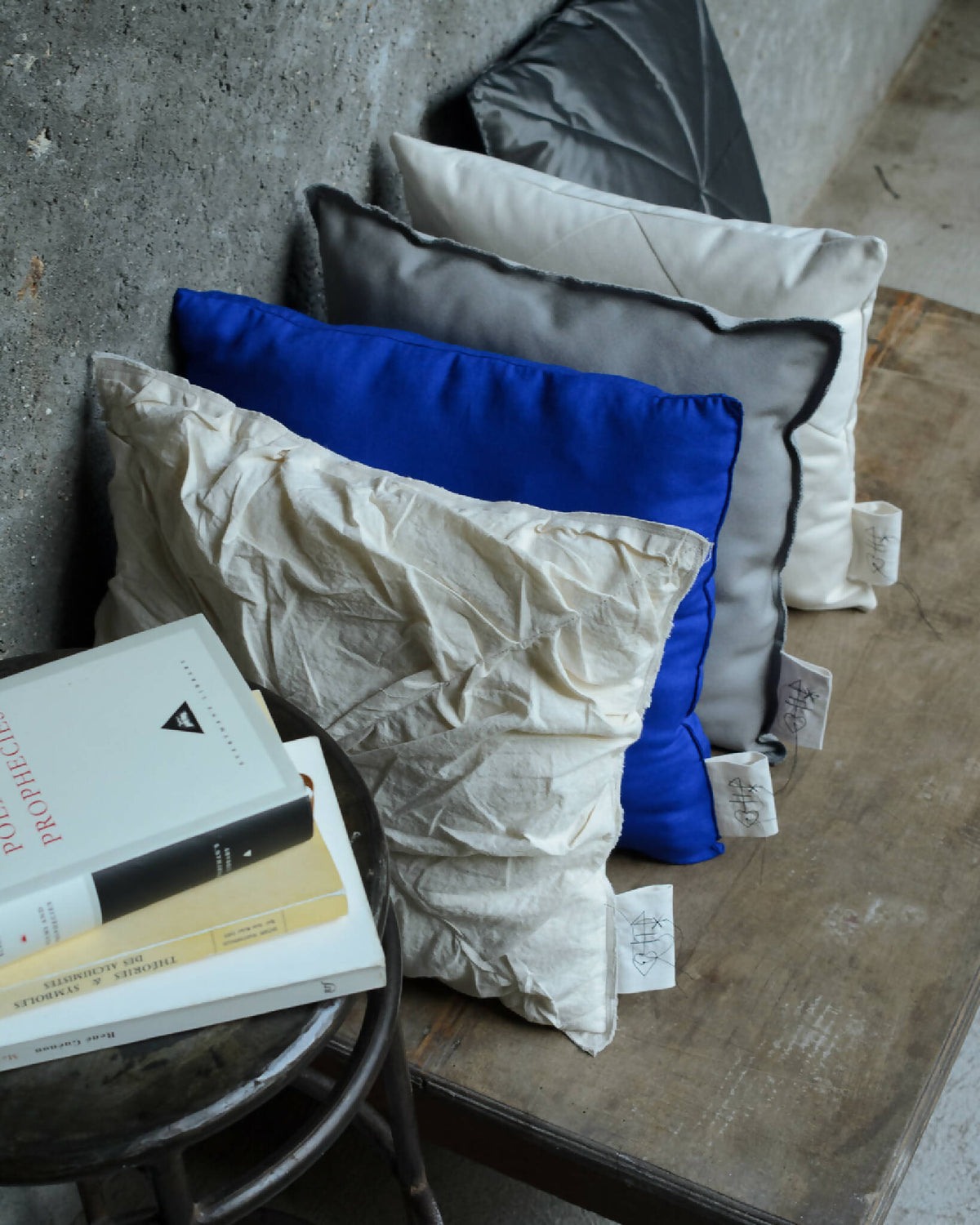 Coussin bleu au centre, parmi d’autres coussins gris et noir, étiquettes visibles