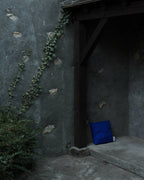 Coussin bleu dans une niche murale sombre, étiquette visible sur le côté