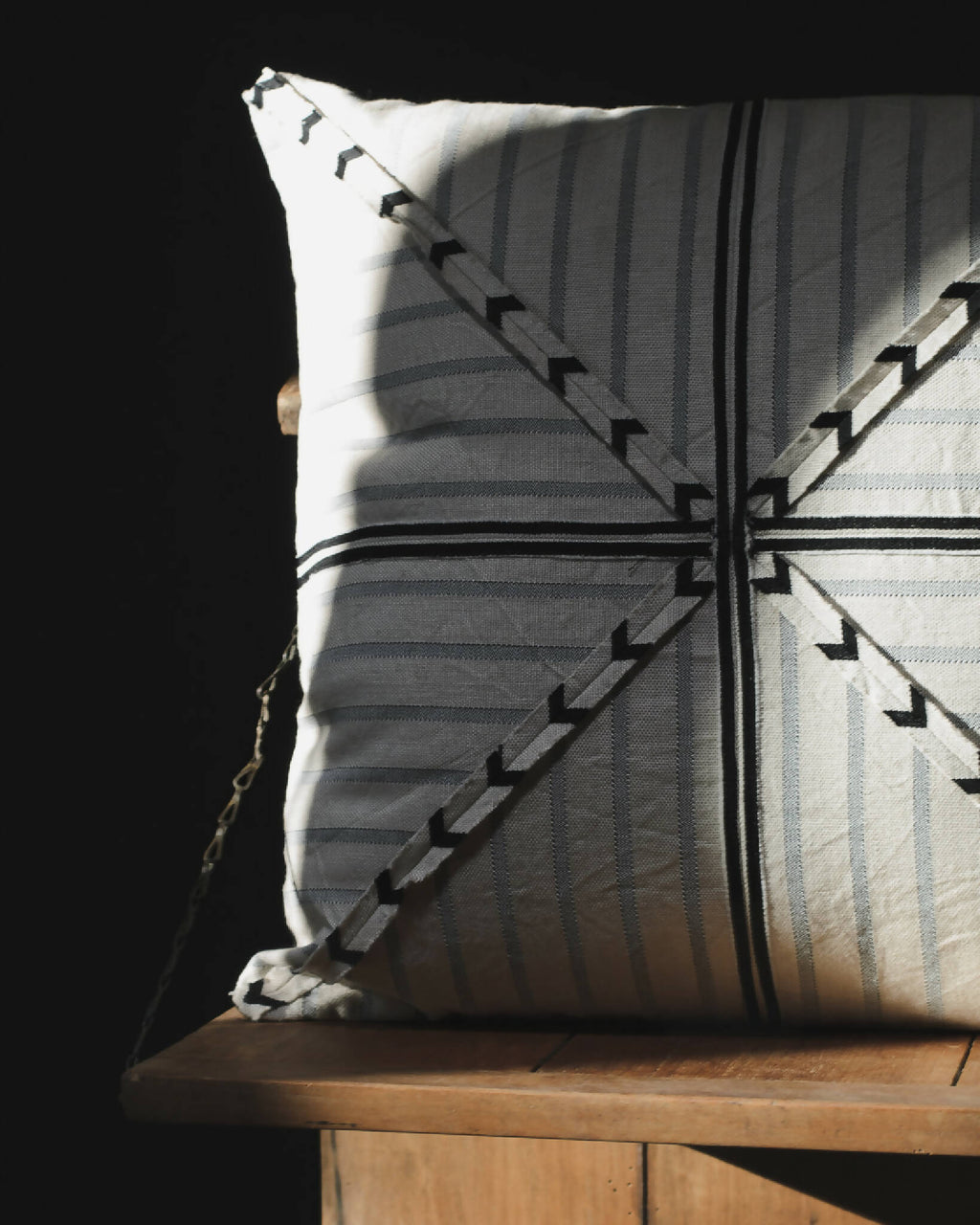 Coussin rectangulaire à rayures bleu-gris, motifs fléchés noirs et point central.