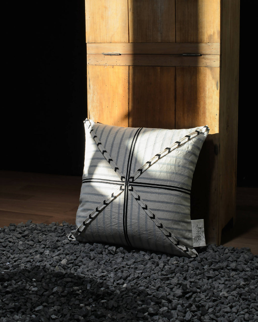 Coussin rayé beige et bleu-gris, motif fléché noir en croix, vue en diagonale.