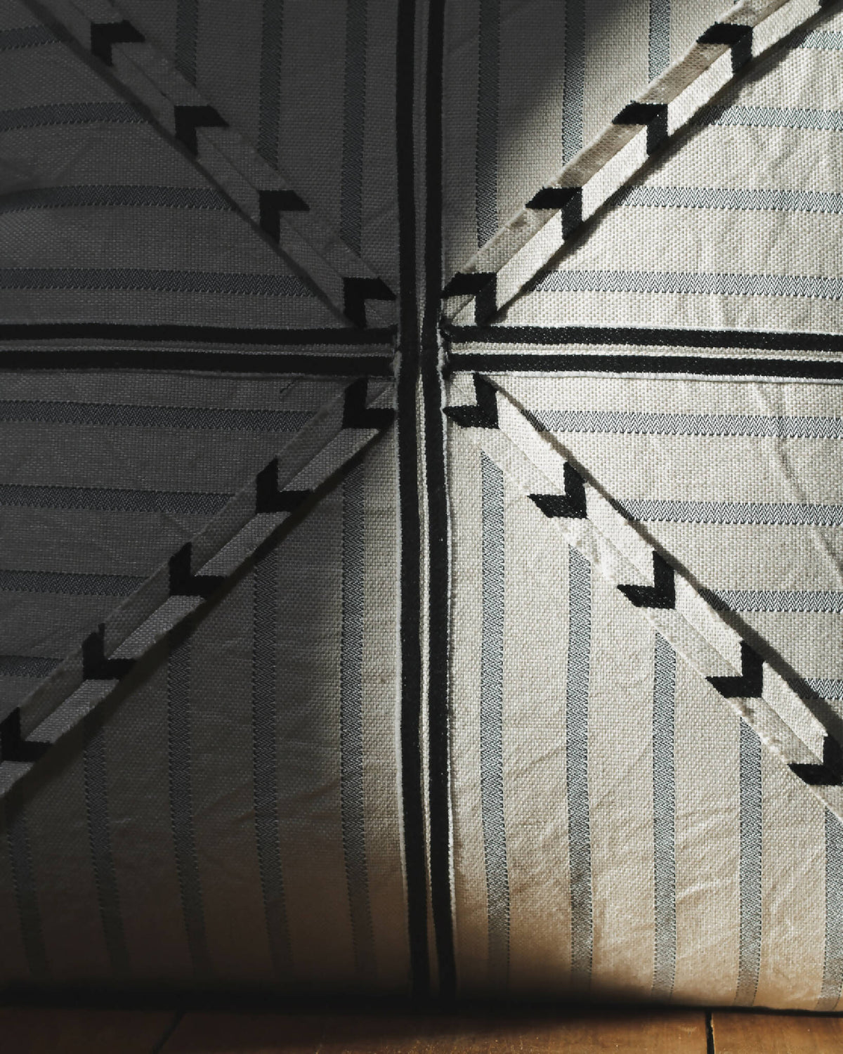 Coussin rayé beige et bleu-gris, lignes verticales et flèches noires au centre.