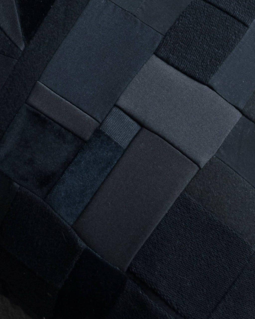 Détail d’un coussin noir en patchwork de carrés, coutures visibles et relief matelassé