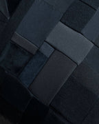 Détail d’un coussin noir en patchwork de carrés, coutures visibles et relief matelassé