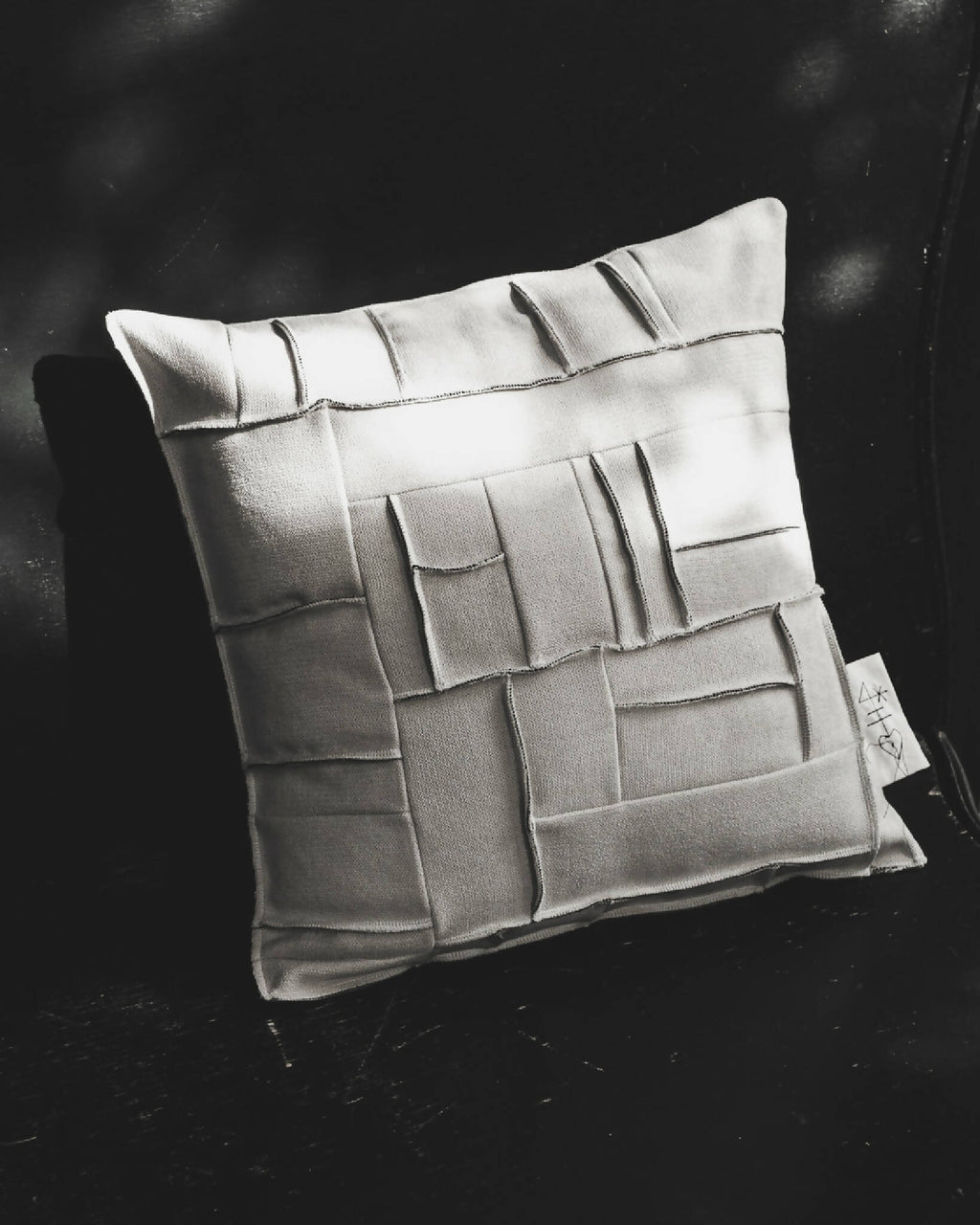 Coussin carré ivoire à reliefs géométriques façon briques, coutures décoratives.