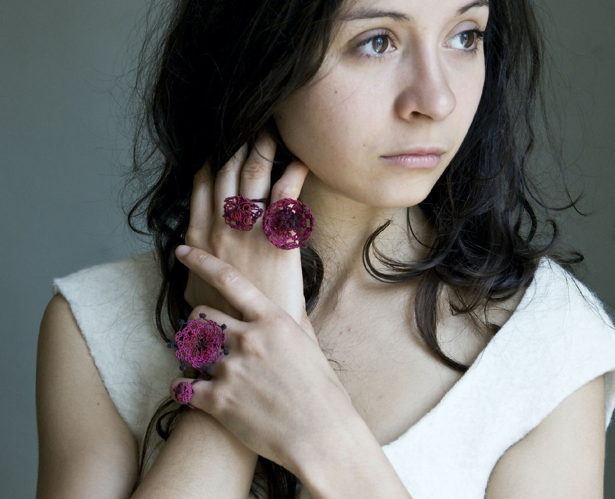 Bague en soie trèfle rouge, forme florale au centre noir, portée sur l’index