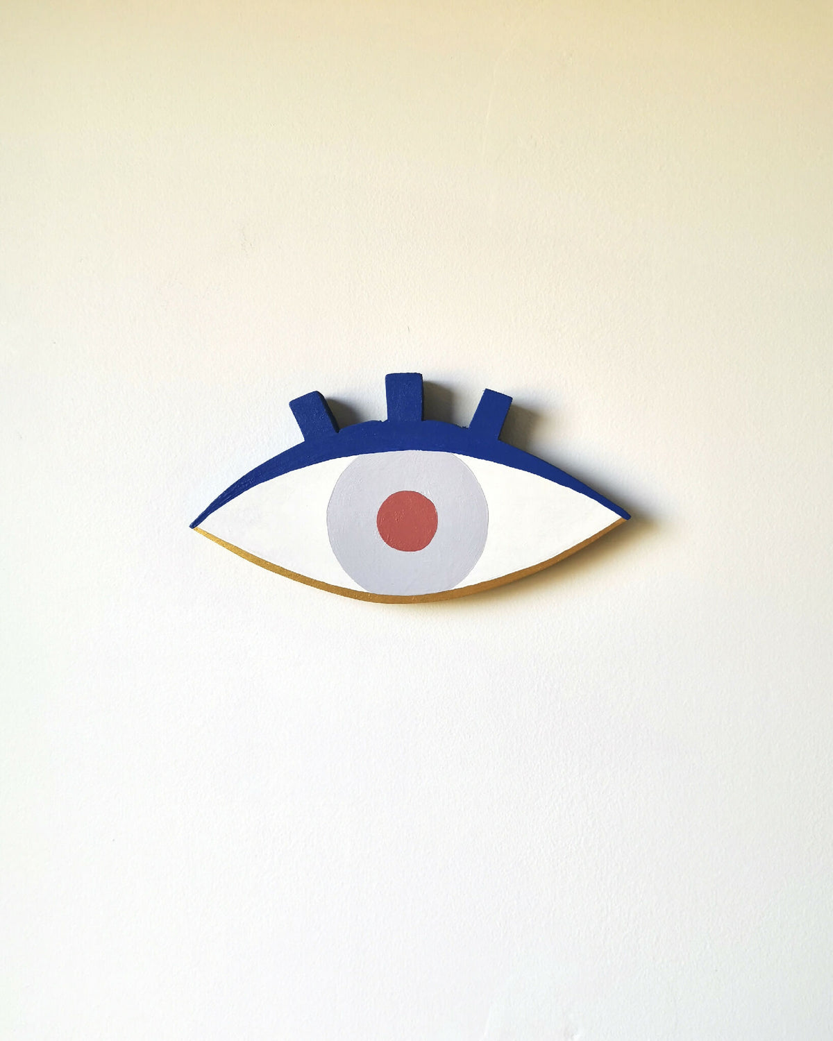 Petit œil en bois peint, contour bleu foncé, iris bleu clair et pupille orange.