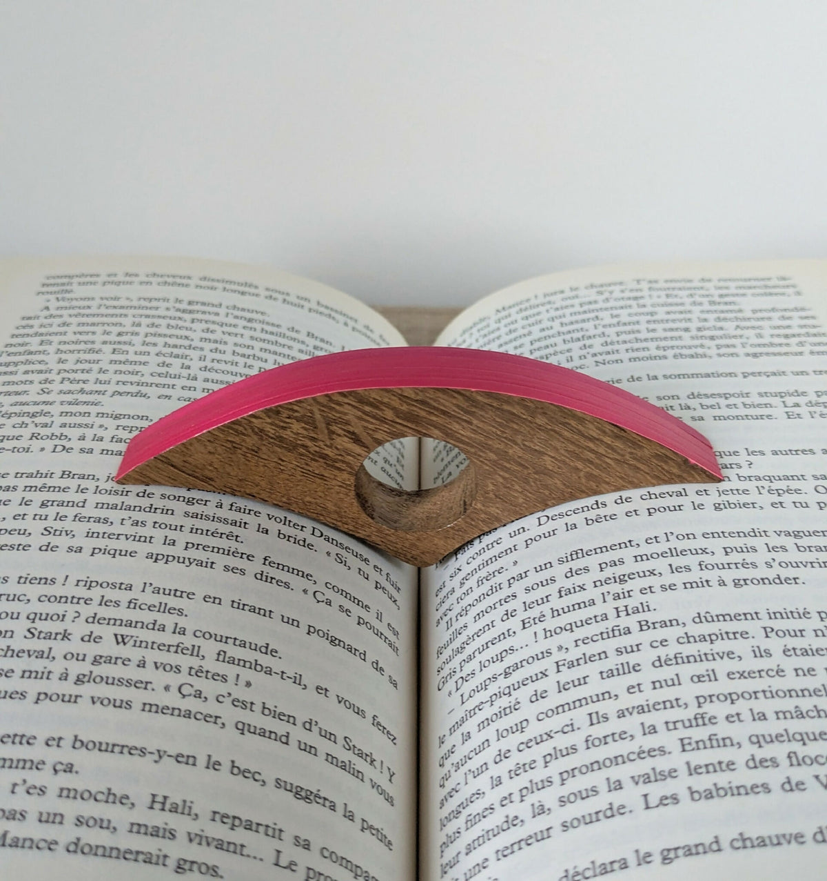 Bague de lecture en marqueterie rose posée sur un livre ouvert, vue de dessus