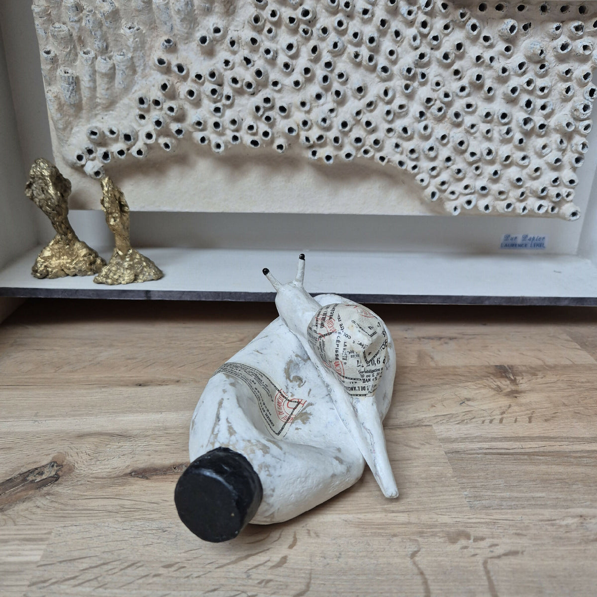 Sculpture d’escargot blanc allongé, coquille noire et corps texturé à motifs.