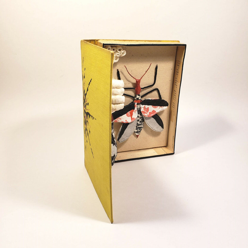 Livre jaune sculpté, intérieur beige avec insecte en relief et éléments papier.