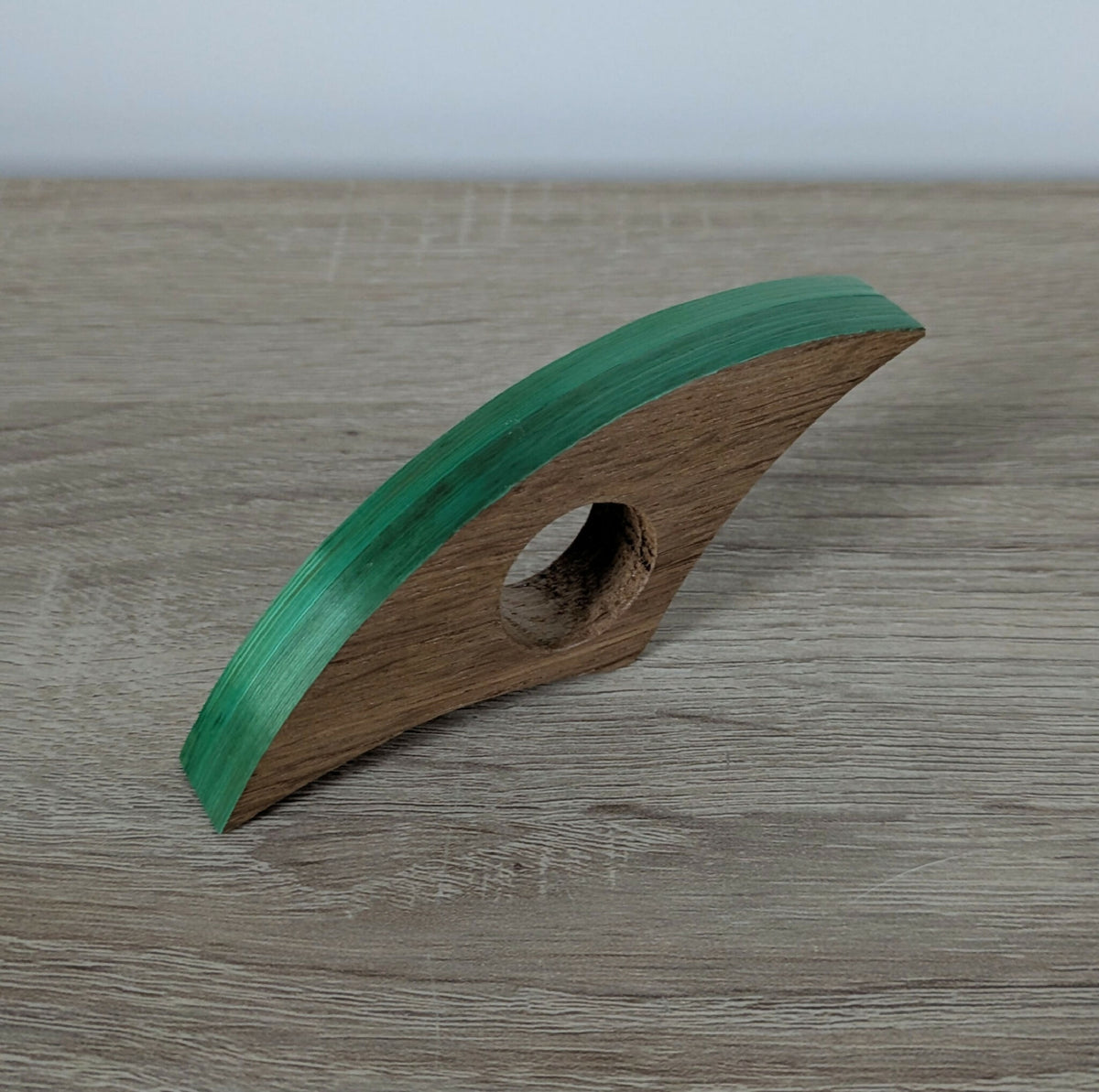 Marque-page en bois avec liseré vert et ouverture ovale, sur table.