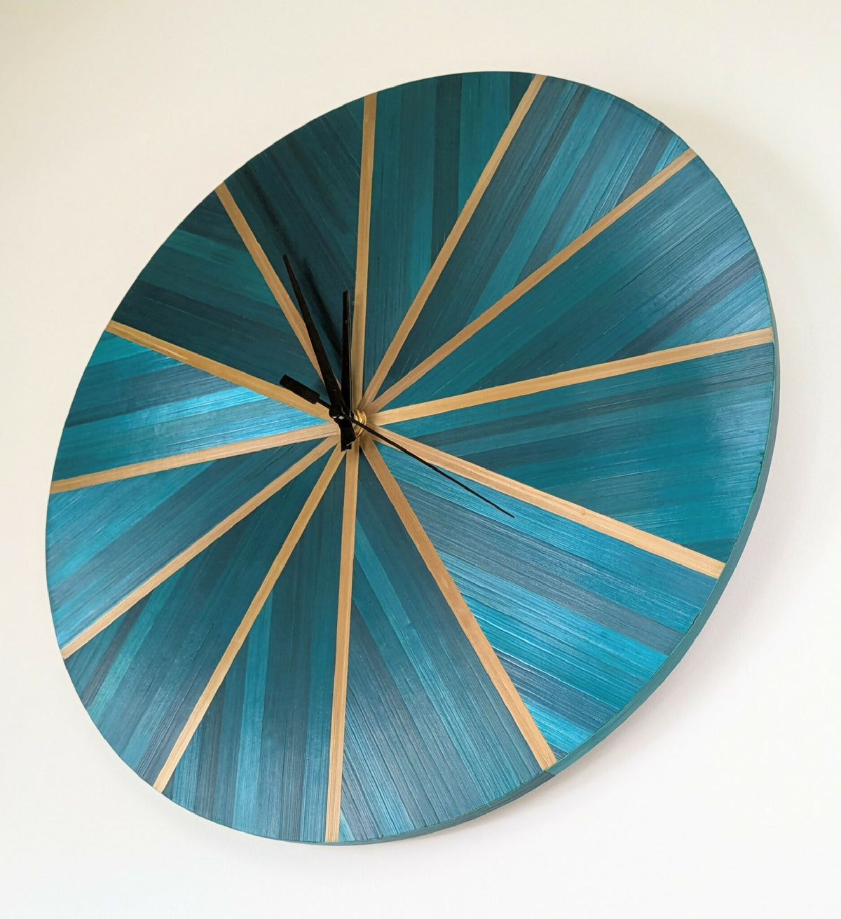 Horloge murale ronde bleu-vert, rayons en paille dorée, mécanisme central et aiguilles noires