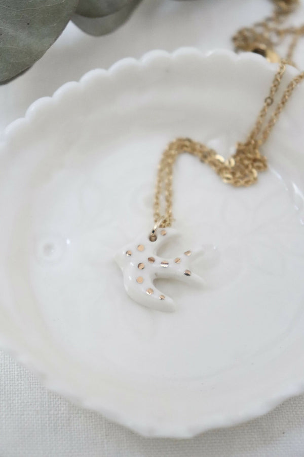 Collier avec pendentif hirondelle en porcelaine blanche et chaîne dorée.