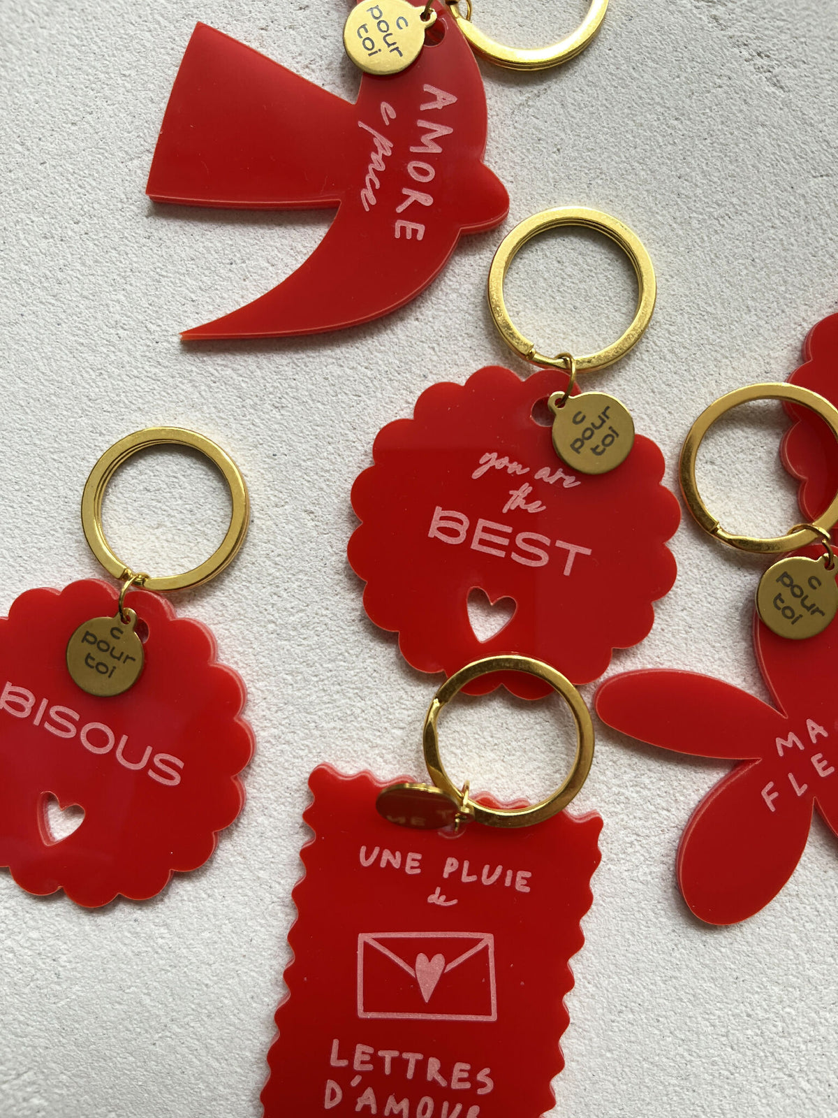 Porte-clés rouges avec anneaux dorés, formes cœurs et inscriptions, dont «BISOUS»
