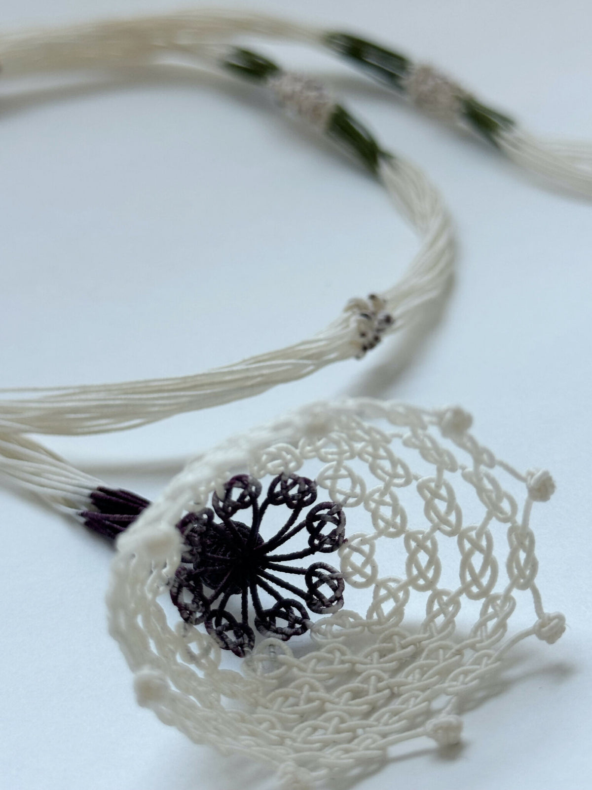 Collier en soie avec pendentif rond blanc, centre noir et franges aux extrémités.