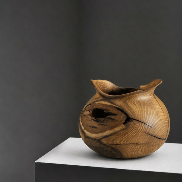 Vase en bois sculpté, forme organique avec ouverture noire sur le dessus.