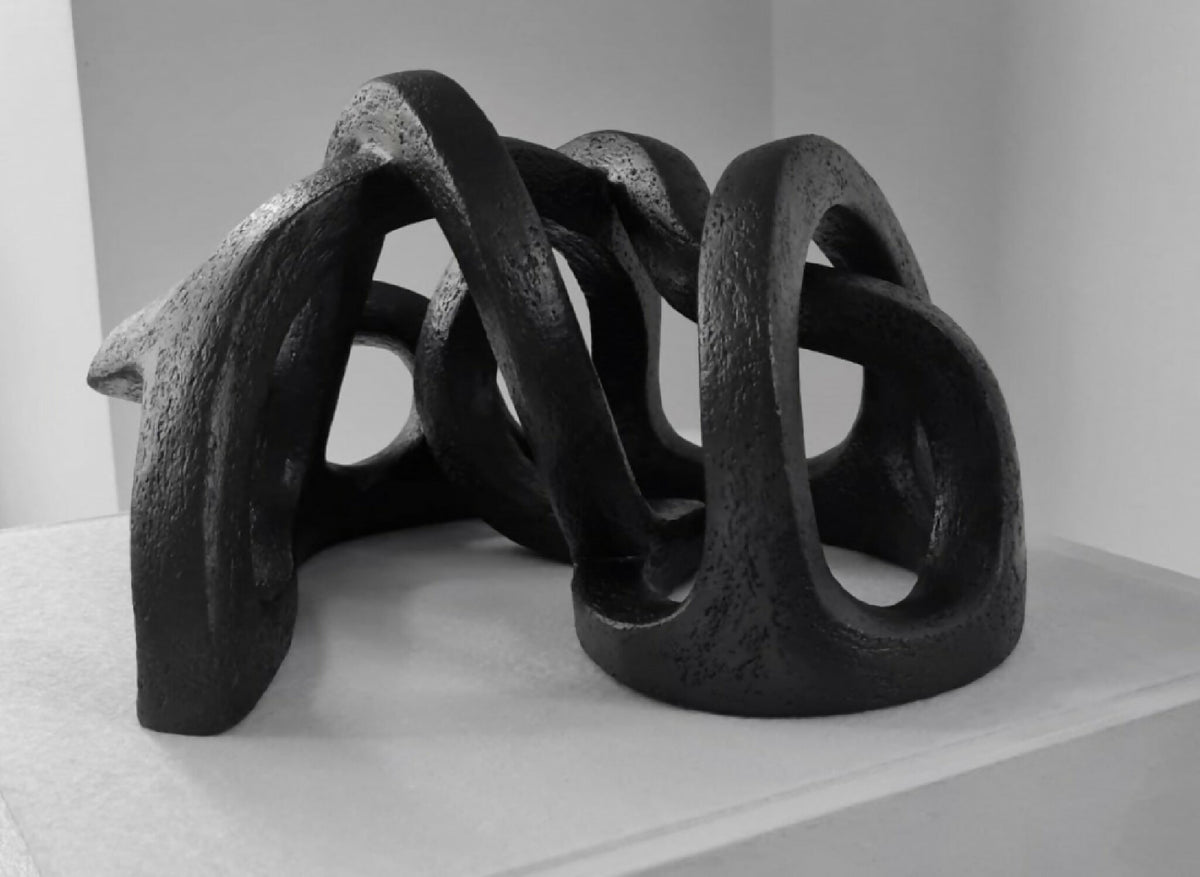 Sculpture abstraite en argile sombre, courbes entrelacées et appuis au sol.