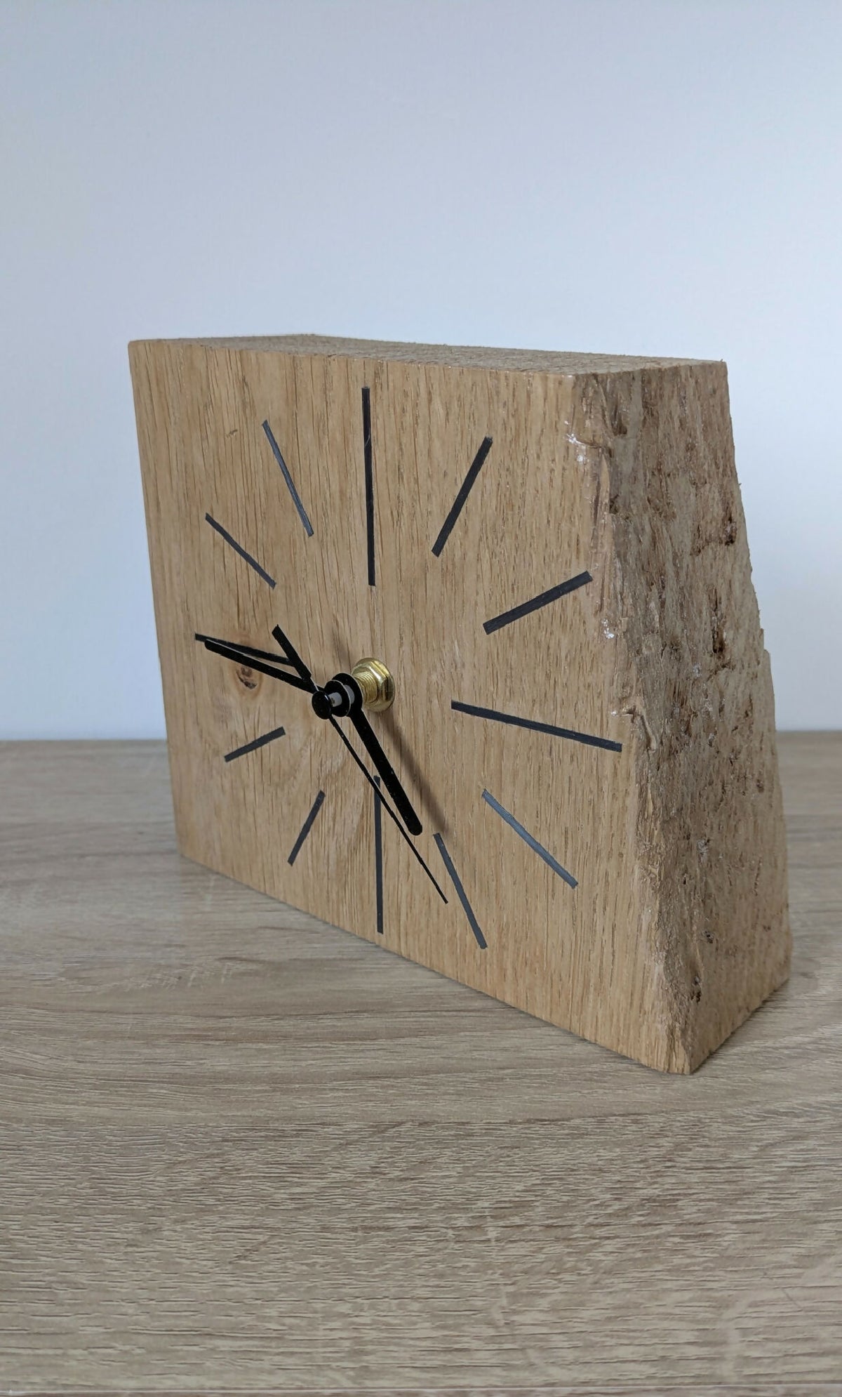Horloge de bureau en chêne, vue en biais : cadran à repères noirs, aiguilles dorées.