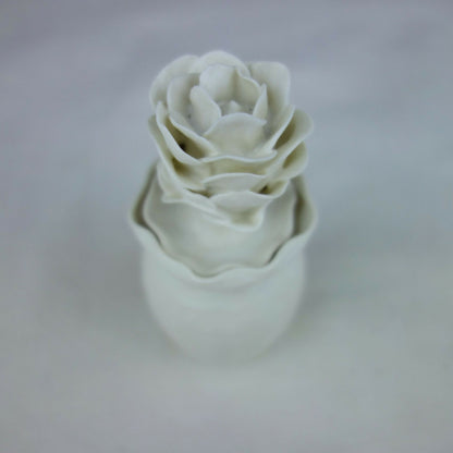 Vase en céramique blanc, fleurs en relief empilées, vue inclinée rapprochée.