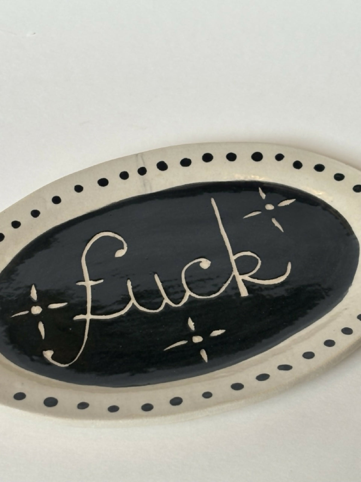 Assiette ovale noire avec texte 'fuck' doré, liseré de pois et détails étoiles.