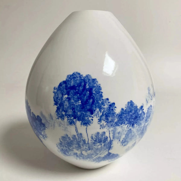 Vase en céramique goutte blanche avec paysage bleu et arbres.