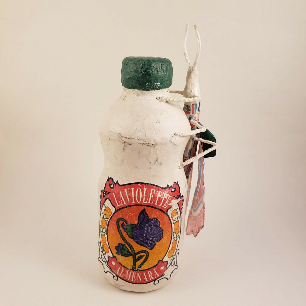 Sculpture posée sur une bouteille en tissu, capuchon vert, étiquette imprimée, rubans multicolores