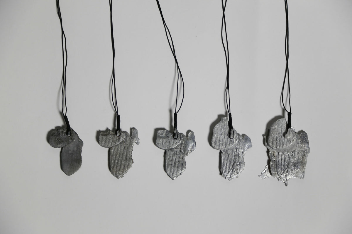 Lot de pendentifs gris en forme de feuille d’arbre, sur cordons noirs.