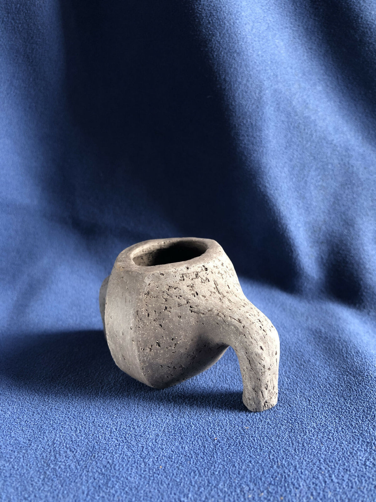 Petit pot en pierre grise avec poignée latérale, ouverture ovale sur le dessus.