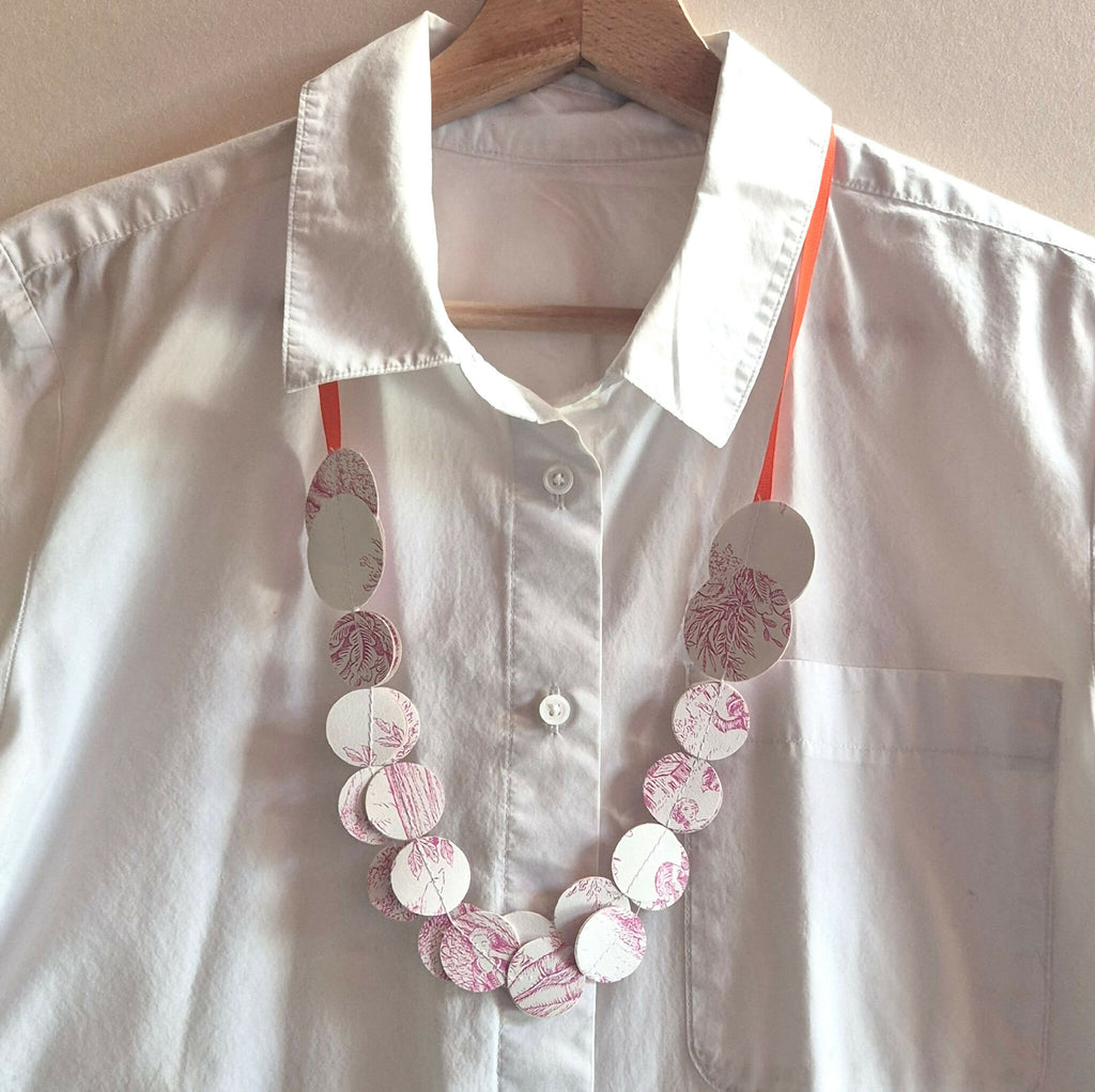 Collier en disques ronds blancs, gris et roses à motifs, sur chemise blanche