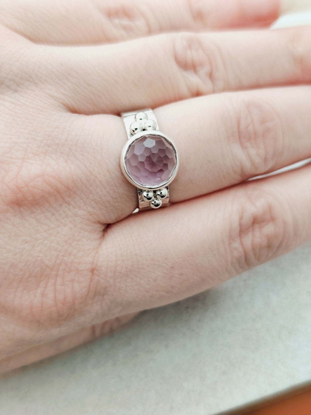 Bague argentée à pierre améthyste ovale facettée, monture ornée de petites billes.